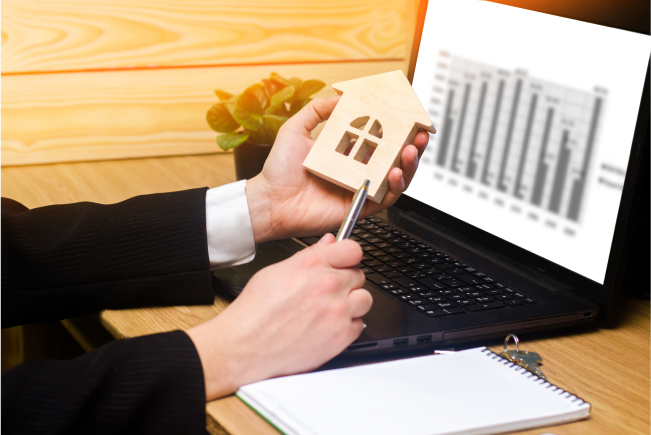 real-estate-agent-holds-house-model-signs-fills-documents-sitting-laptop-1.png